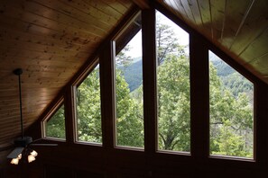 A room with large windows offering a view of a forested mountain area.