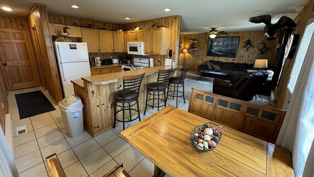 A kitchen with wooden cabinets, a refrigerator, a microwave, a stove, and a dining area with a table and chairs. - 40 Creek Lodge South at Waubay Lake (Grenville)