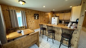 A wooden-paneled kitchen with a dining area, bar stools, and a refrigerator. - 40 Creek Lodge South at Waubay Lake (Grenville)