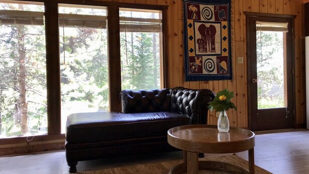 L’intérieur d’un chalet en bois, avec un canapé en cuir, une table basse ronde en bois et une tapisserie au mur.