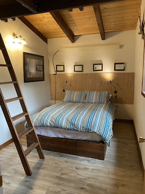 Un dormitorio con escalera de madera, cama con ropa de cama a rayas y cuadros en la pared.