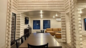 A log cabin interior with a large dining table, chairs, a sofa, and a chandelier.