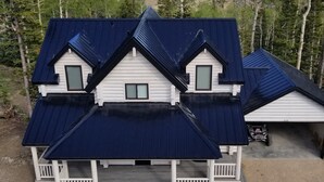 A two-story log cabin with a dark blue metal roof, a front porch, and a garage.