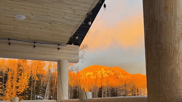 A wooden deck with a railing, overlooking a forested area with autumn-colored trees and a mountain in the background.