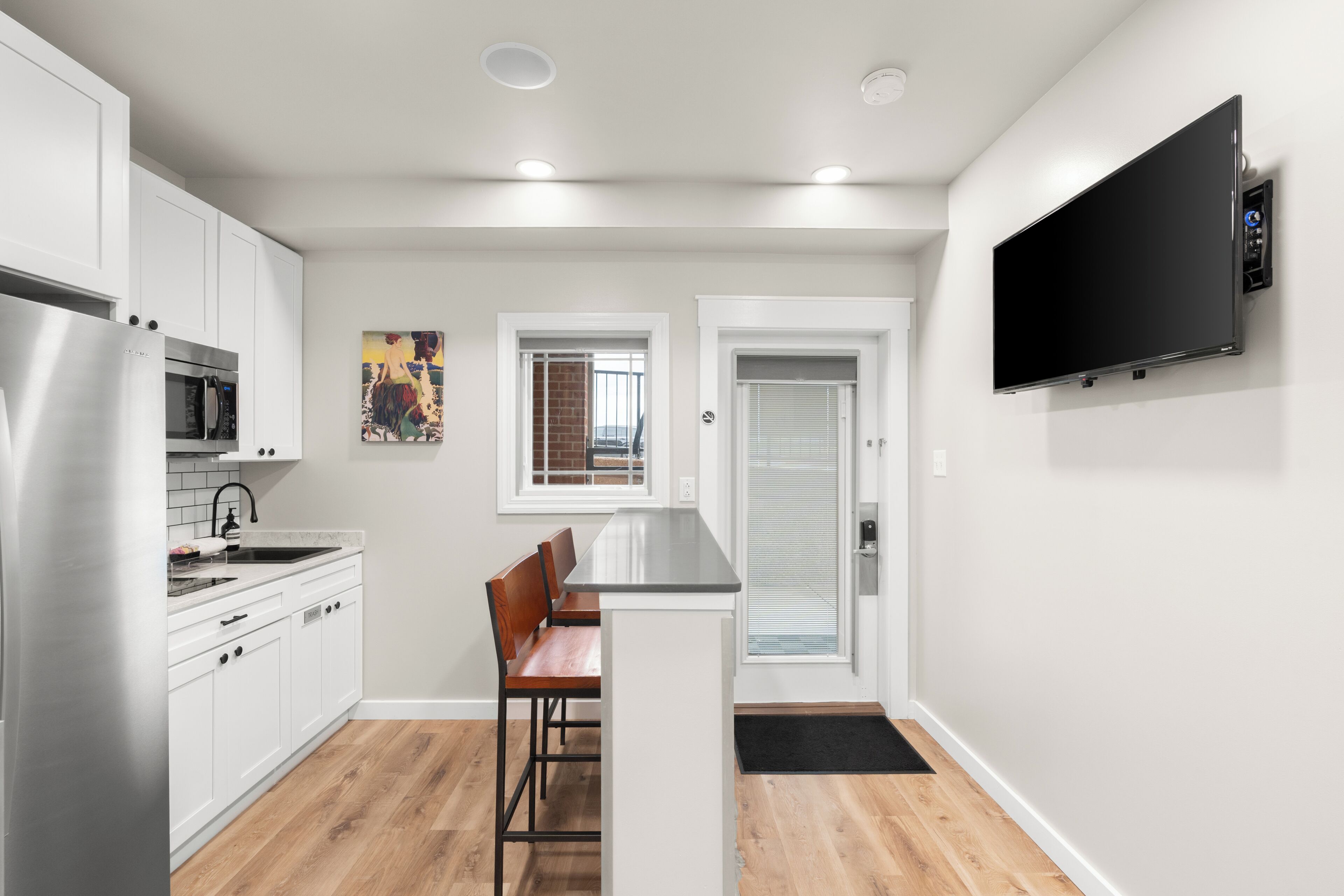 Una cocina moderna con armarios blancos, electrodomésticos de acero inoxidable, un banco de madera y un televisor de pantalla plana montado en la pared.