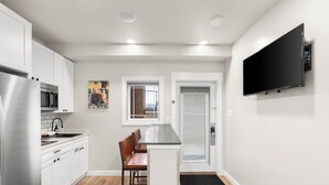 Eine moderne Küche mit weißen Schränken, Edelstahlgeräten, einer Holzbank und einem an der Wand befestigten Flachbildfernseher.