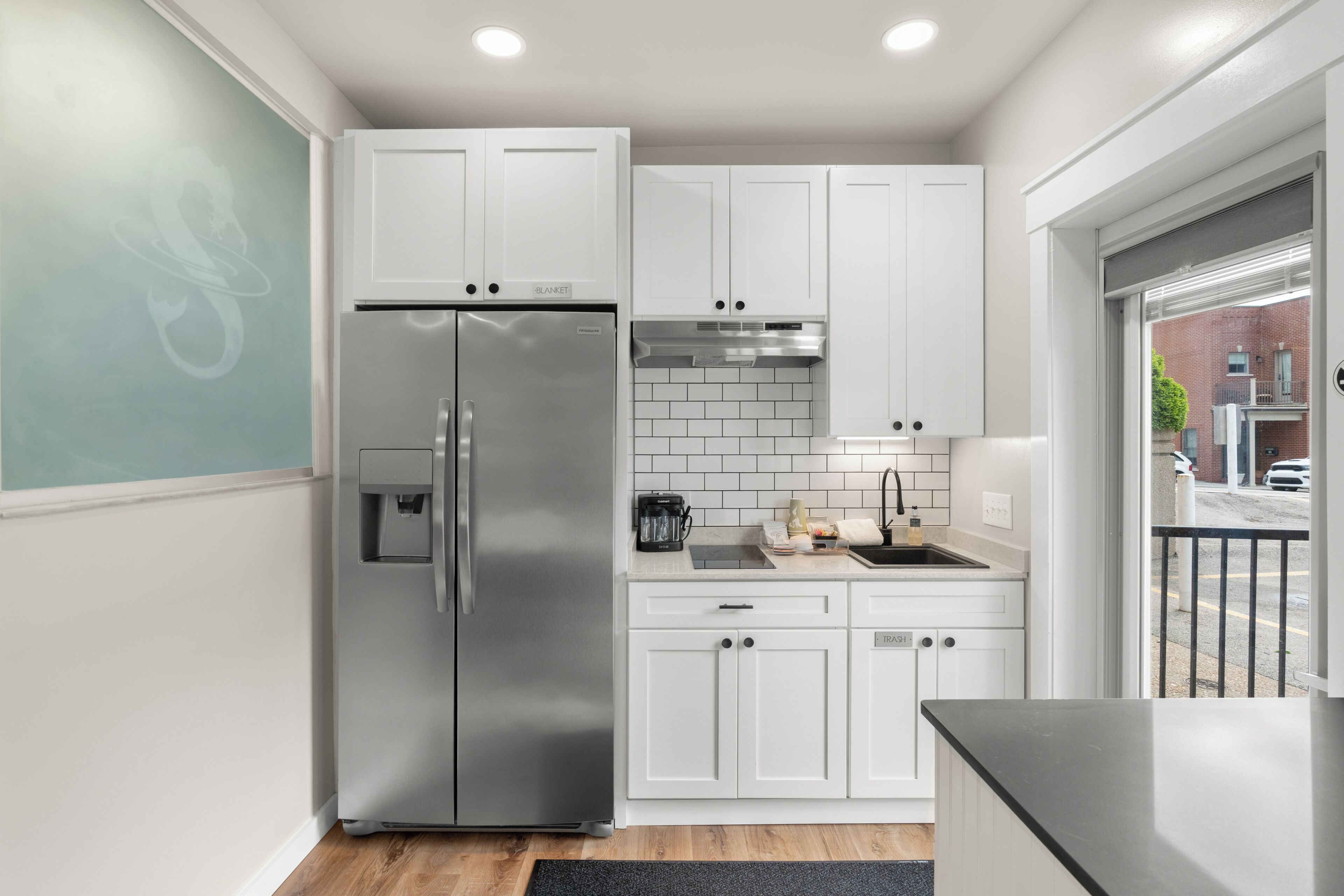 A modern kitchen with white cabinets, a stainless steel refrigerator, and a black countertop.