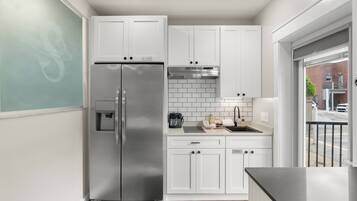 A modern kitchen with white cabinets, a stainless steel refrigerator, and a black countertop.