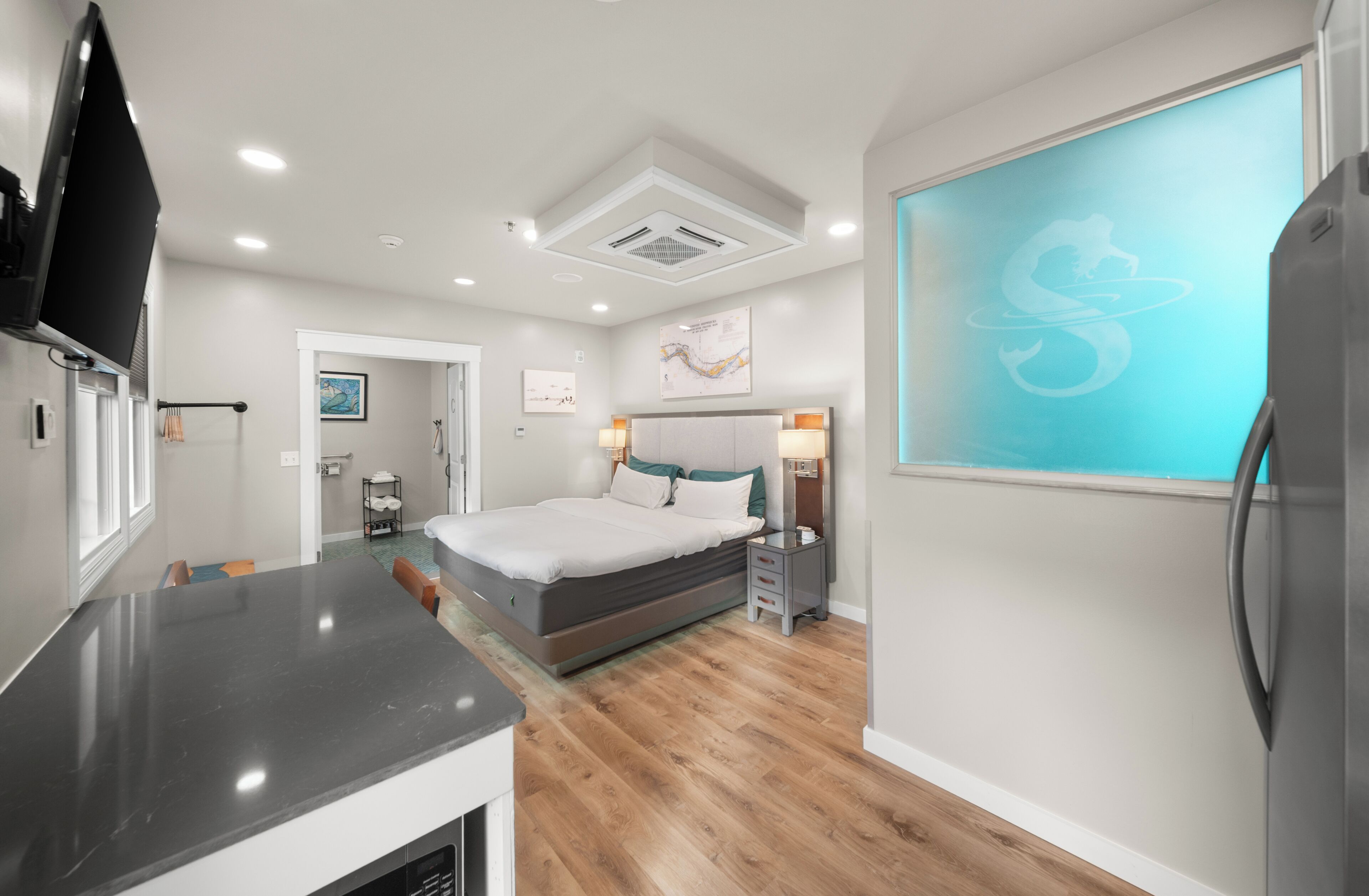 Quarto de hotel moderno com cama, mesa de cabeceira e uma janela grande.