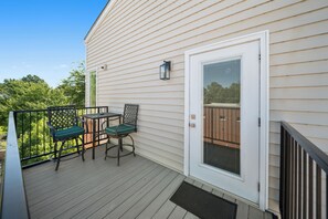 A balcony with a table and two chairs, a door with a window, and a railing. - River Sirens Hotel (Washington)