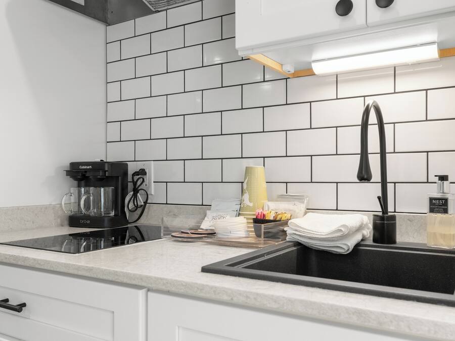 A modern kitchen with a black sink, white cabinets, and a tiled backsplash.