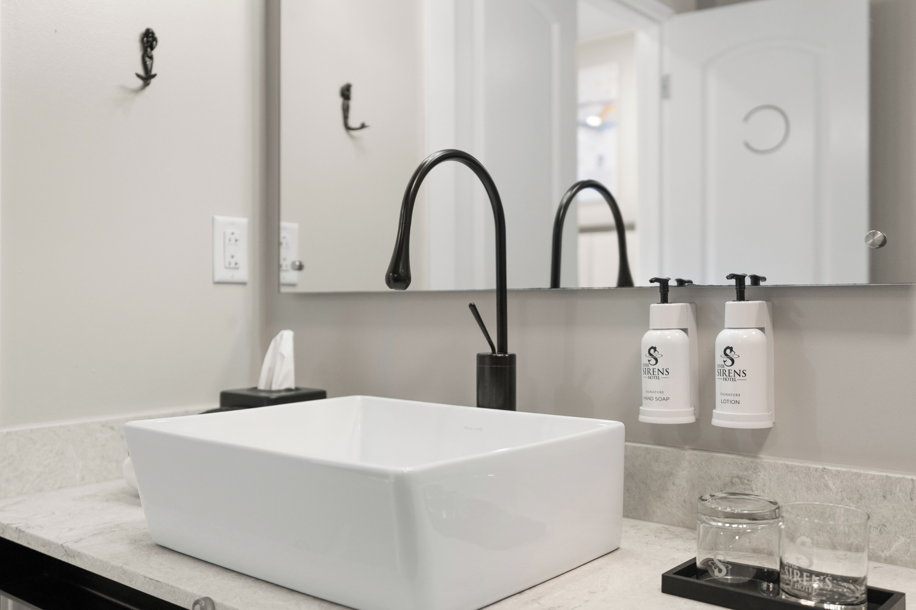 Baño con lavamanos blanco, grifo negro y dos botellas de jabón de manos y loción.