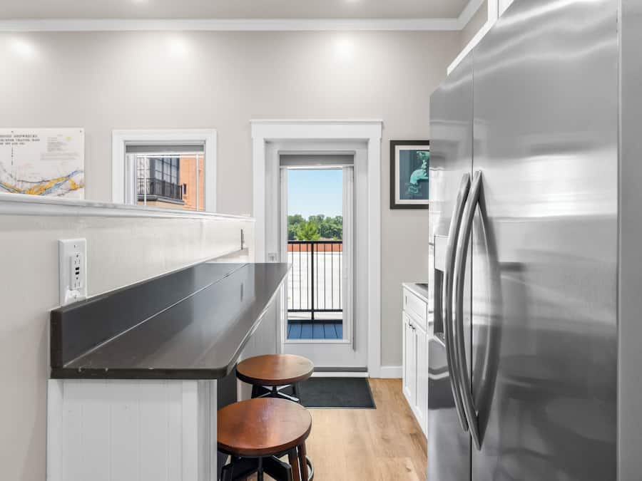 A modern kitchen with a stainless steel refrigerator, a black countertop, and two stools.