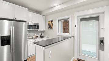 A modern kitchen with stainless steel appliances, white cabinetry, and a black countertop.