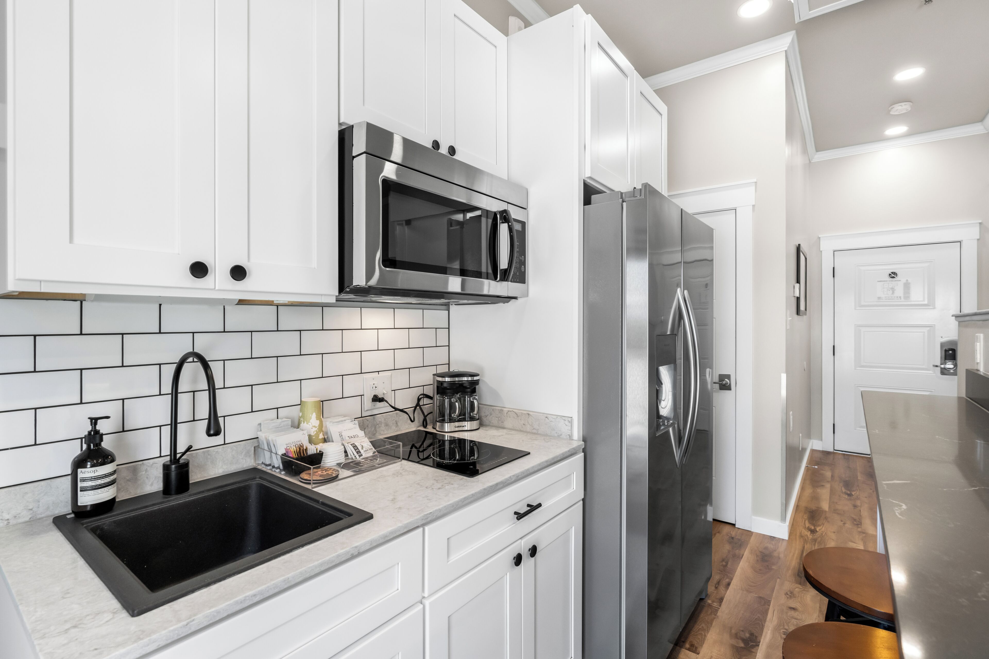 A modern kitchen with white cabinetry, a stainless steel refrigerator, a black sink, and a coffee maker.