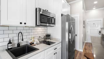 A modern kitchen with white cabinetry, a stainless steel refrigerator, a black sink, and a coffee maker.