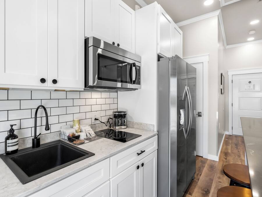 A modern kitchen with white cabinetry, a stainless steel refrigerator, a black sink, and a coffee maker.