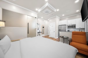 Una habitación de hotel con una cama, escritorio, silla, kitchenette y baño.