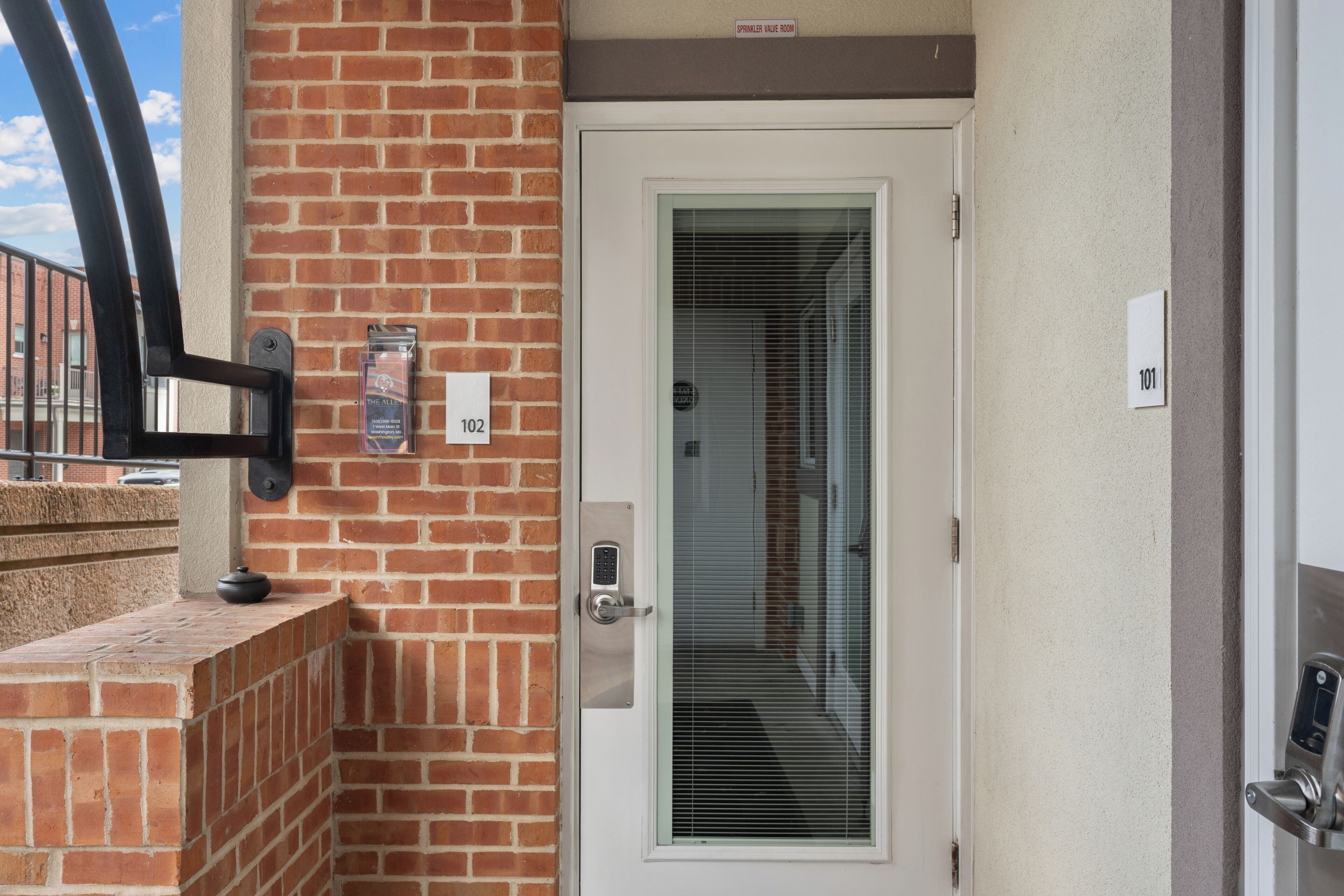 A door with a keypad lock, a brick wall, and a window with blinds.