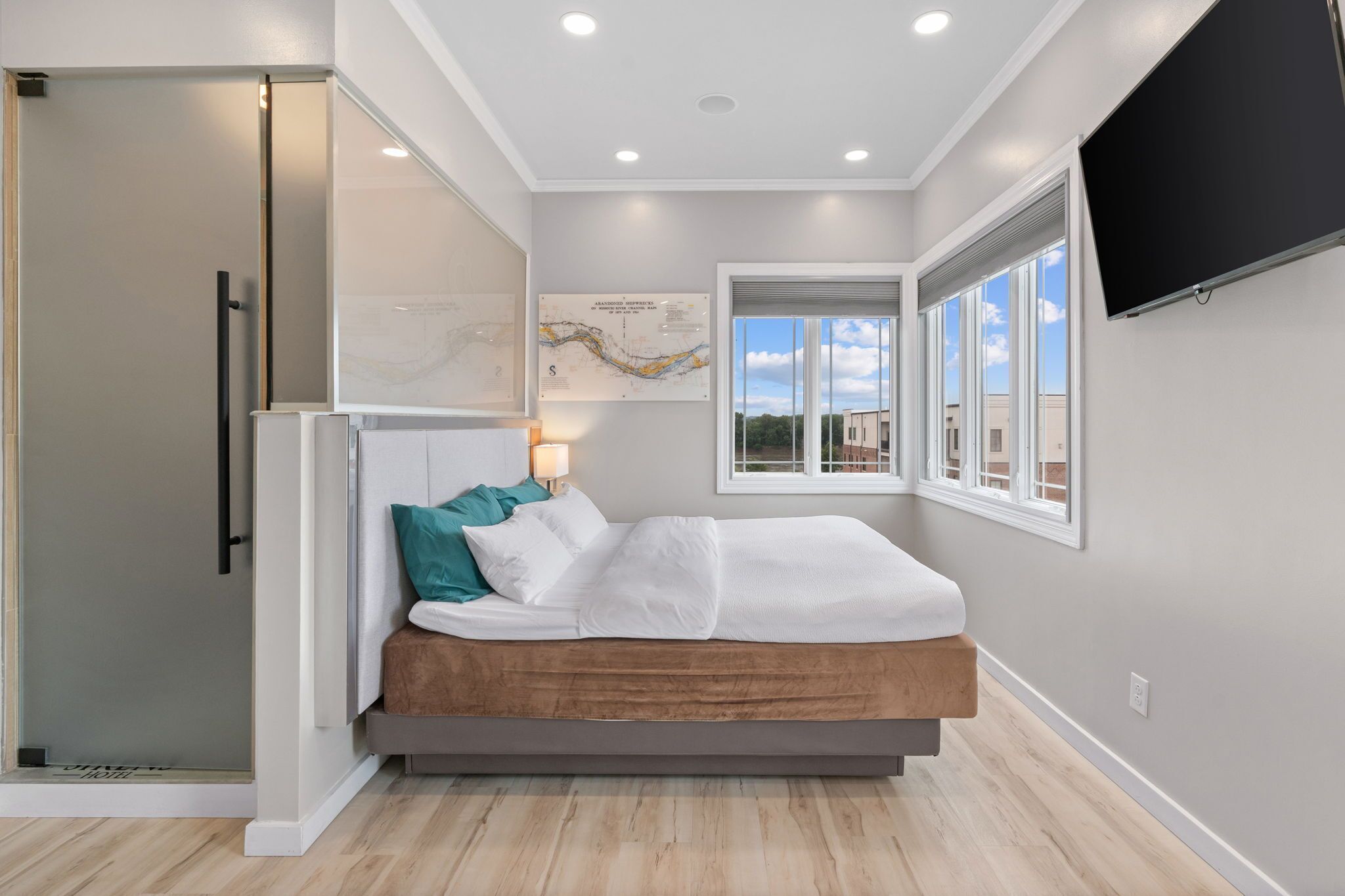 Une chambre à coucher avec un lit, une fenêtre, un téléviseur fixé au mur et une porte.