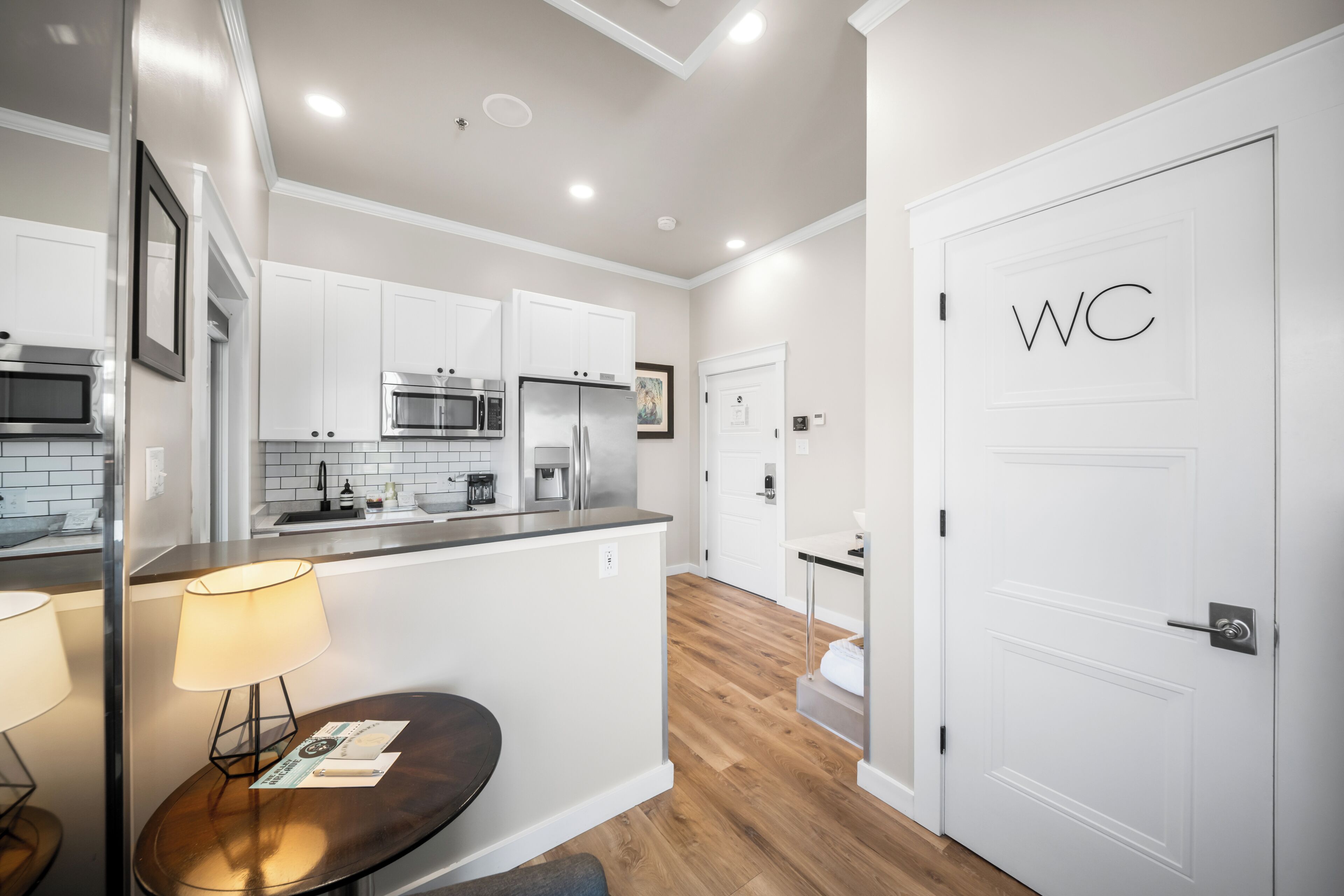 A modern kitchen with white cabinetry, stainless steel appliances, and a wooden floor.