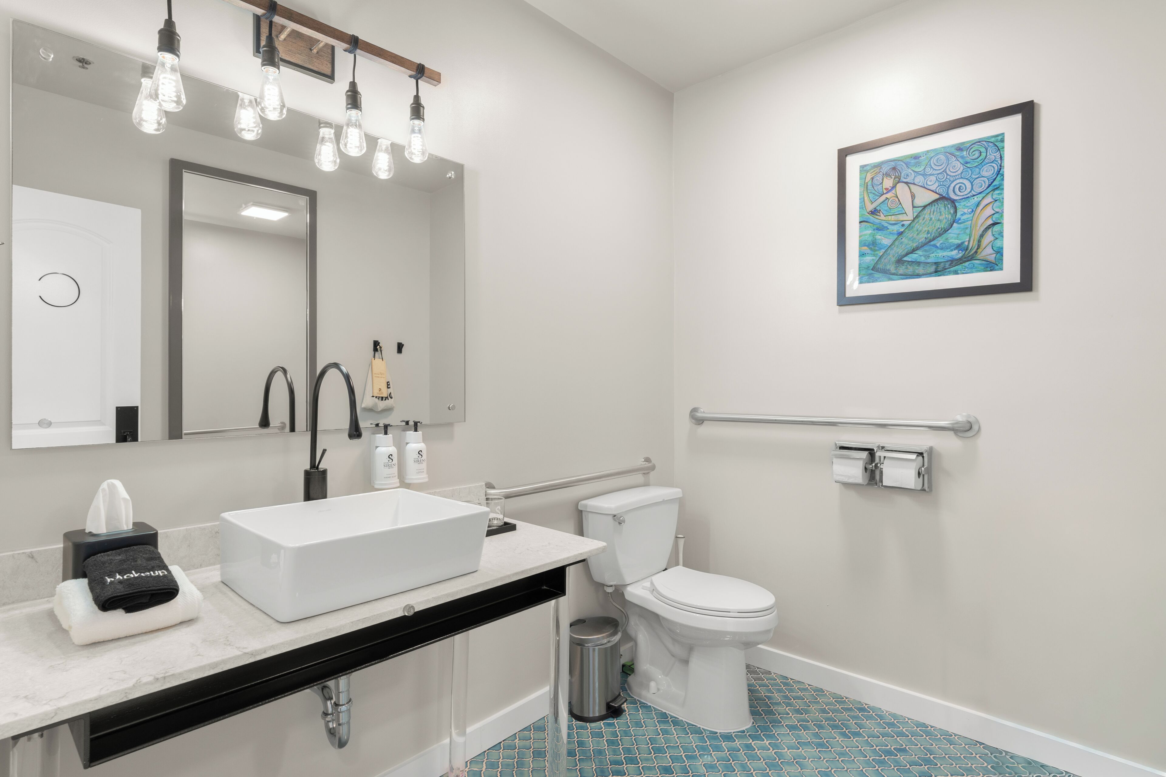 Un bagno moderno con un lavandino bianco, un water, un asciugamani ad aria e un cestino.