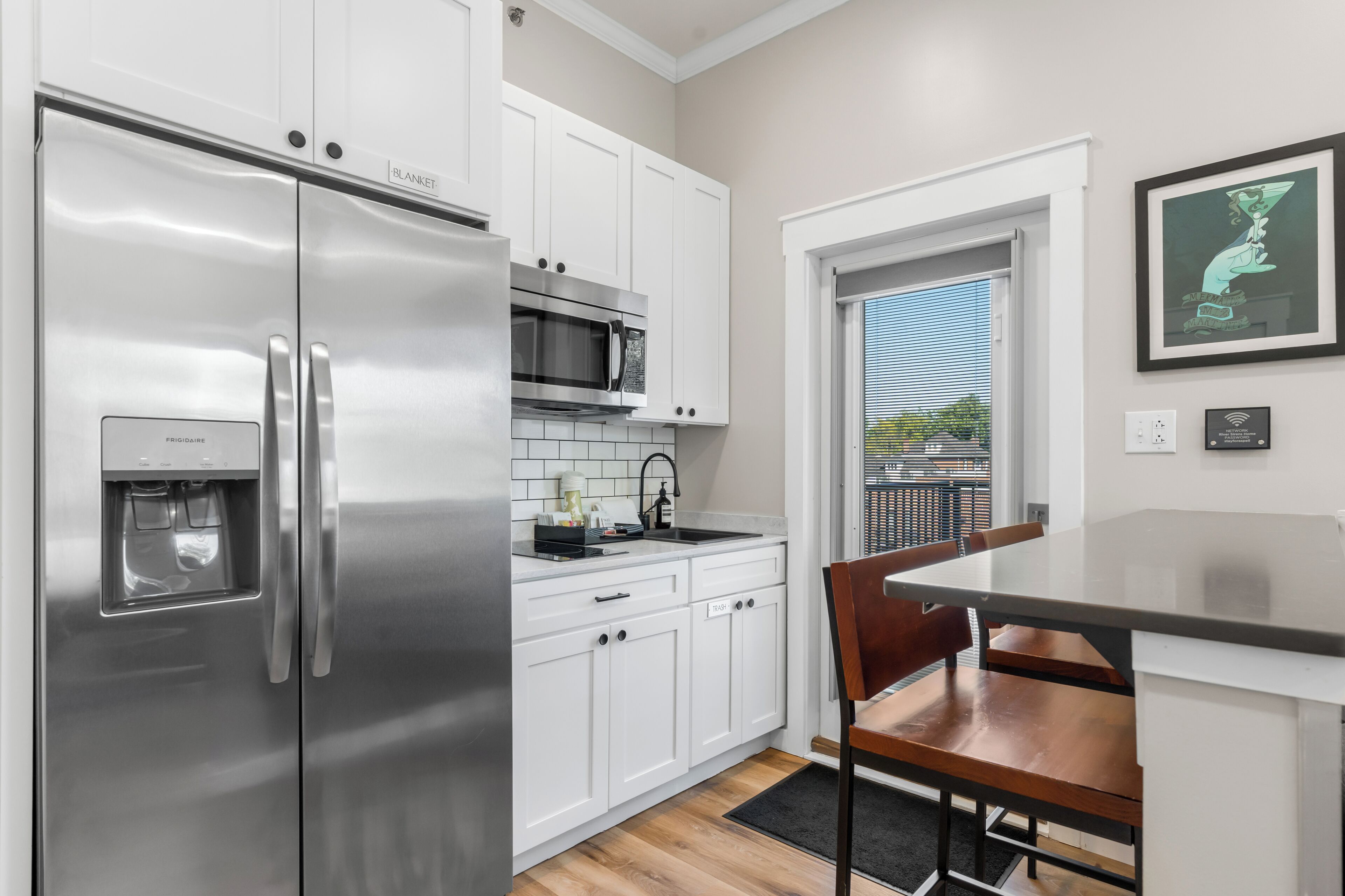 A modern kitchen with stainless steel appliances, white cabinetry, a black countertop, and a dining area with a wooden chair.