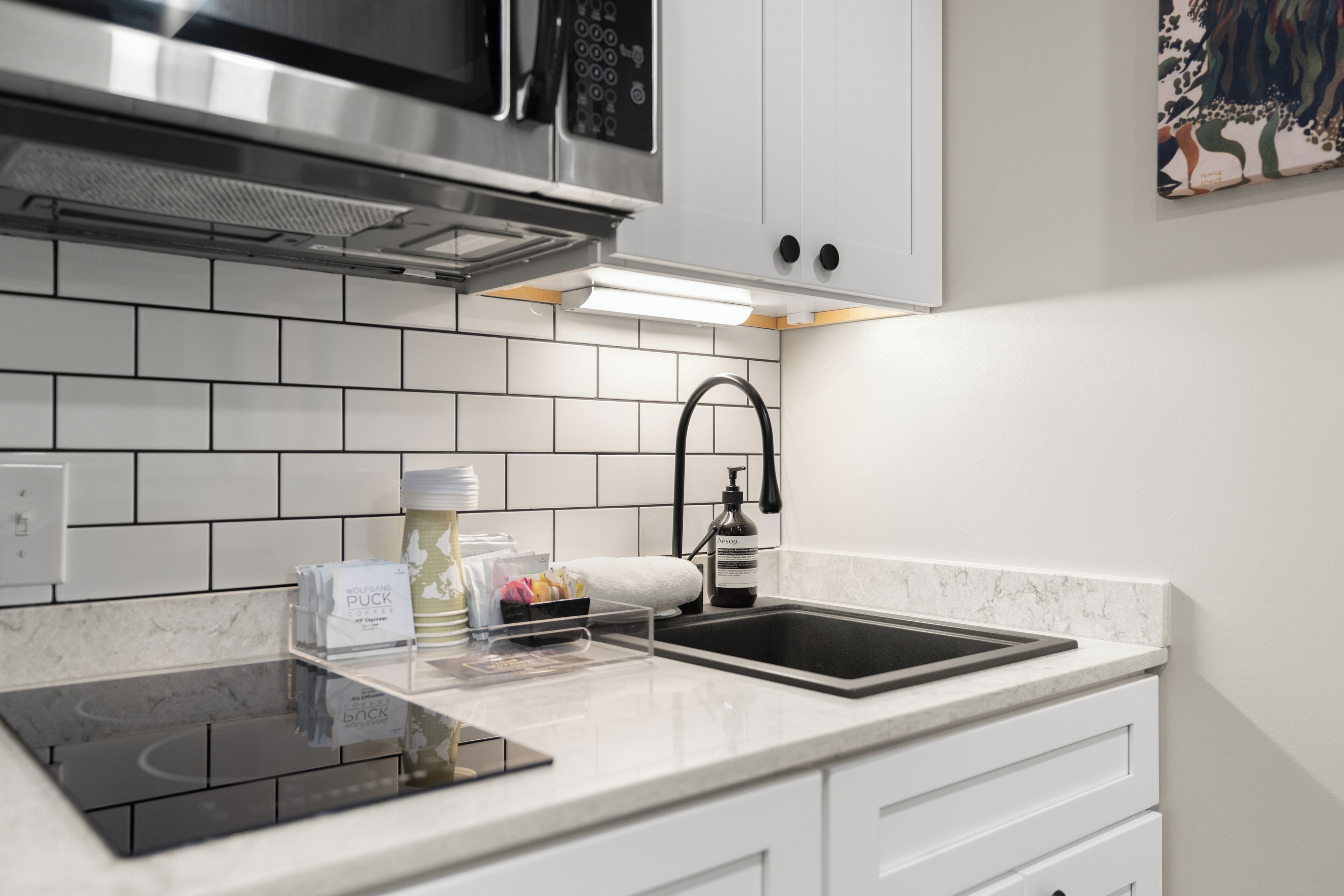 Una cocina moderna con armarios blancos, una campana de acero inoxidable, un grifo negro y una placa de inducción integrada.