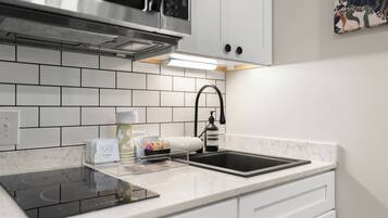 Una cocina moderna con armarios blancos, una campana de acero inoxidable, un grifo negro y una placa de inducción integrada.