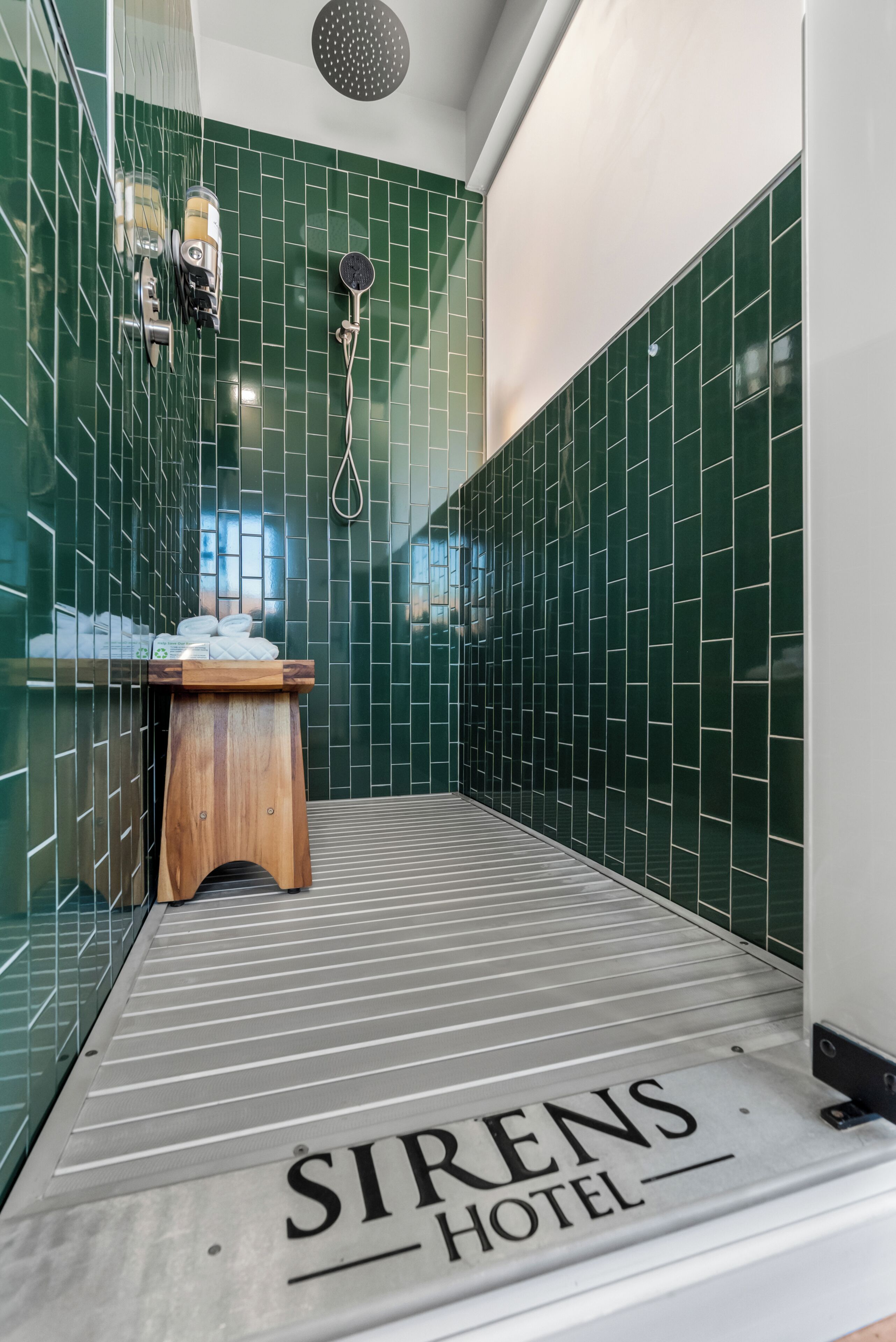 Casa de banho de hotel com azulejos verdes, um chuveiro e um banco de madeira.