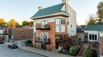 A two-story building with a green roof, a brick facade, and a small balcony with outdoor seating.