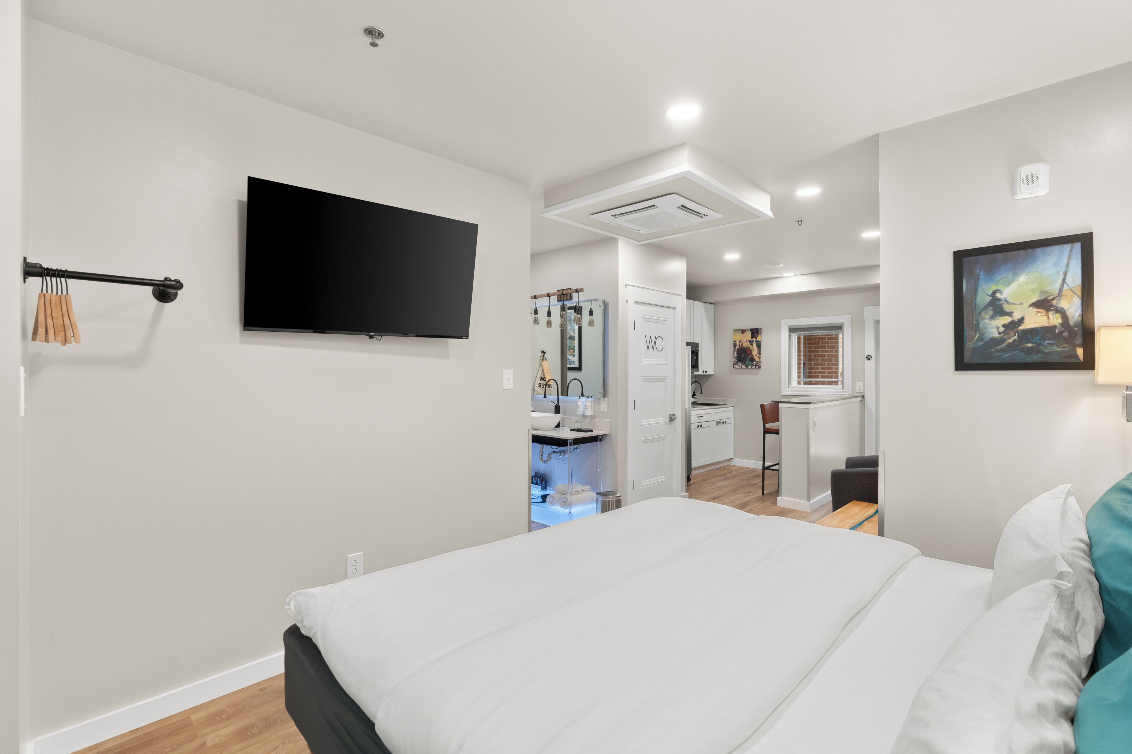 A modern bedroom with a large bed, a flat-screen TV mounted on the wall, and a bathroom visible through an open door.