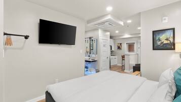 A modern bedroom with a large bed, a flat-screen TV mounted on the wall, and a bathroom visible through an open door.