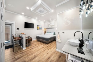 Una habitación de hotel moderna con cama, escritorio, silla, televisor y baño con lavamanos y espejo.
