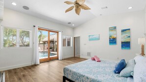 Ein Schlafzimmer mit Bett, Deckenventilator und Blick auf einen Pool durch Glasüren.