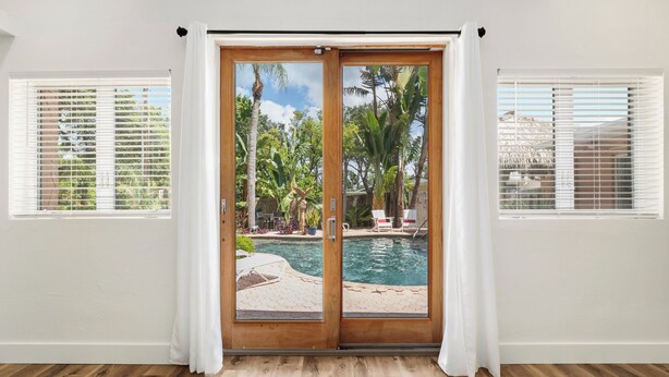 Ein Zimmer mit einer Glasschiebetür, die zu einem Poolbereich führt, weißen Wänden und Holzböden.