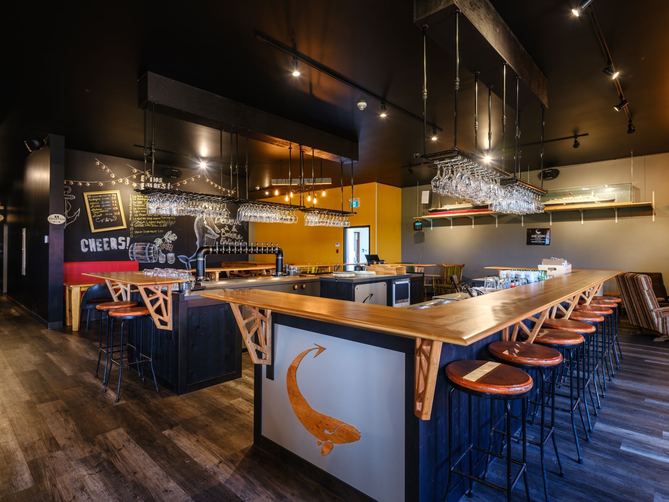 A bar area with a long counter, stools, and hanging lights.