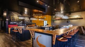 A bar area with a long counter, stools, and hanging lights.