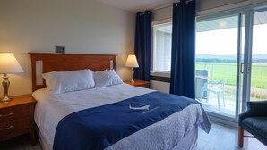 A hotel room with a large bed, two bedside tables with lamps, a window with curtains, and a view of the outdoors.