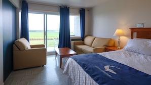 A hotel room with a bed, a sofa, a chair, a table, and a view of the outdoors.