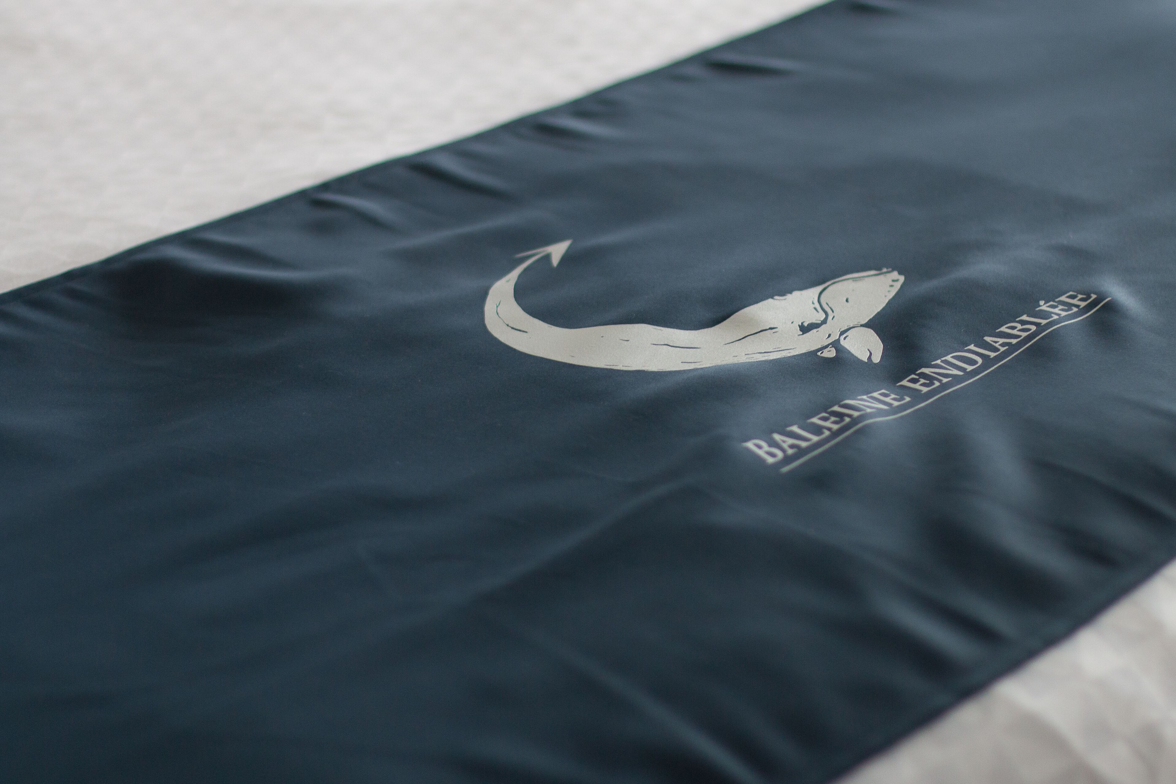 Tela azul oscuro con un gráfico blanco de una ballena y el texto "BALEINE ENDIABLÉE".