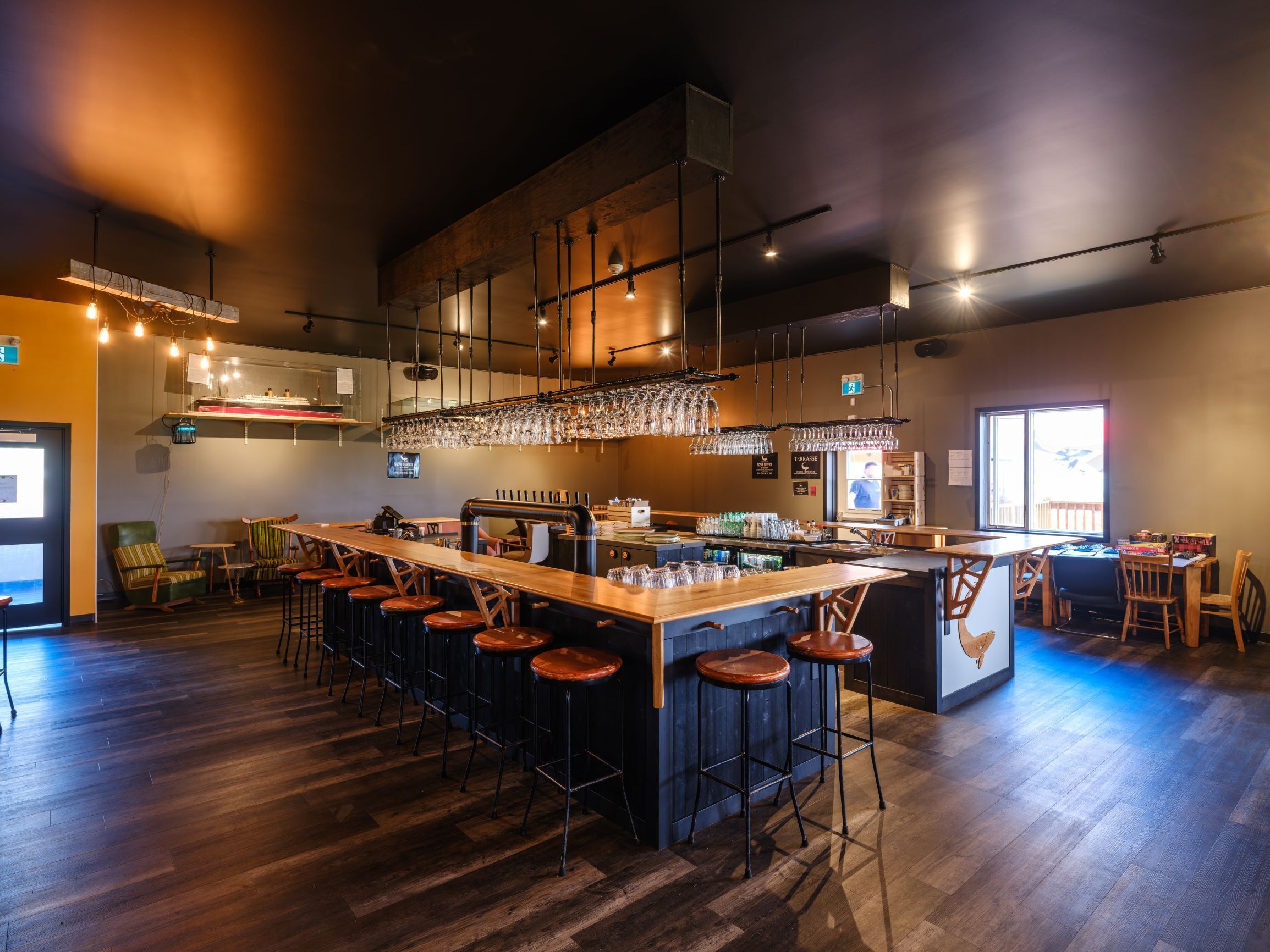 A modern bar with a long counter, stools, and hanging glassware.