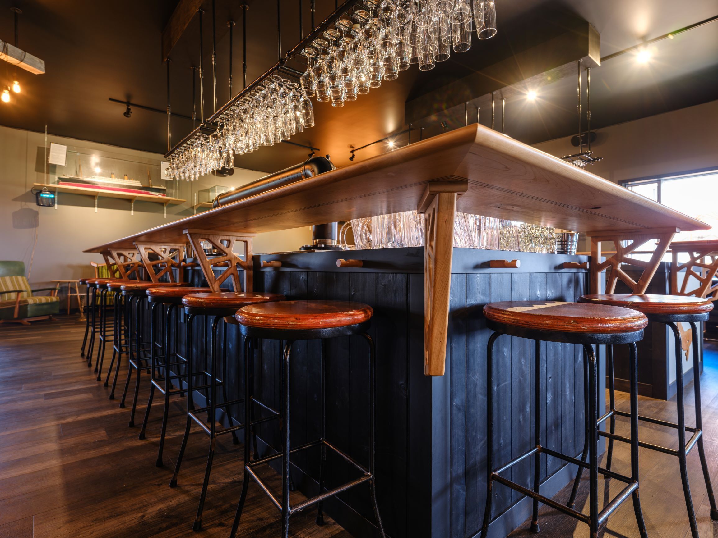 Un espace bar doté de plusieurs tabourets, d’un comptoir en bois et de verres suspendus.