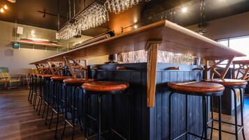 Un espace bar doté de plusieurs tabourets, d’un comptoir en bois et de verres suspendus.