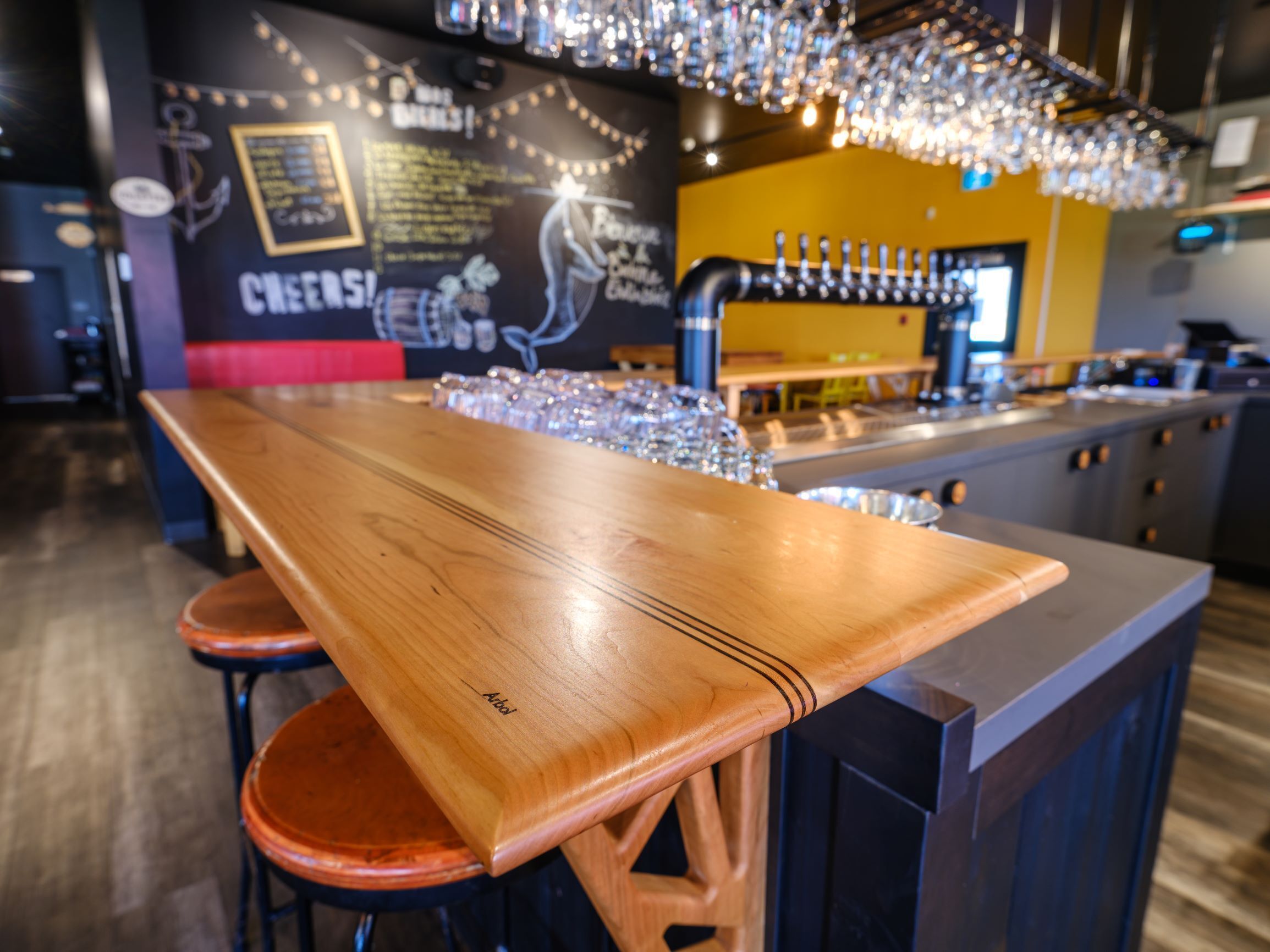 A bar area with a wooden bar counter, stools, and a chalkboard menu.