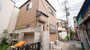 A narrow urban street with a two-story brick building, a wooden fence, and a small garden area. - Ferio101 (Tokyo)