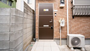 A brown double door with a sign, a brick wall, a tiled entrance, and an air conditioning unit. - Ferio101 (Tokyo)
