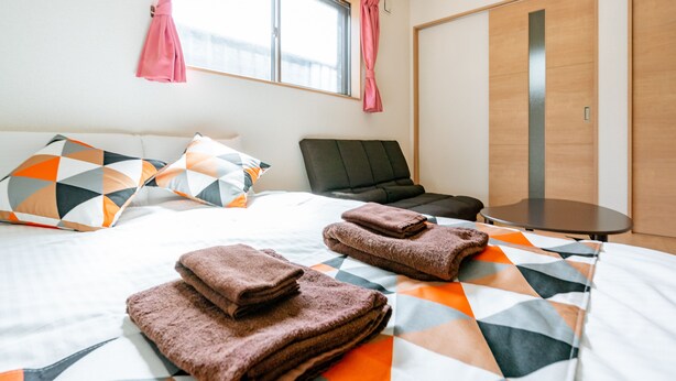 A hotel room with a bed, pillows, a chair, a table, and a wardrobe. - Ferio101 (Tokyo)