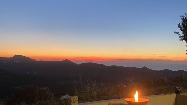 Ein Sonnenuntergang, zu sehen von einer Steinstruktur, im Vordergrund eine brennende Kerze.