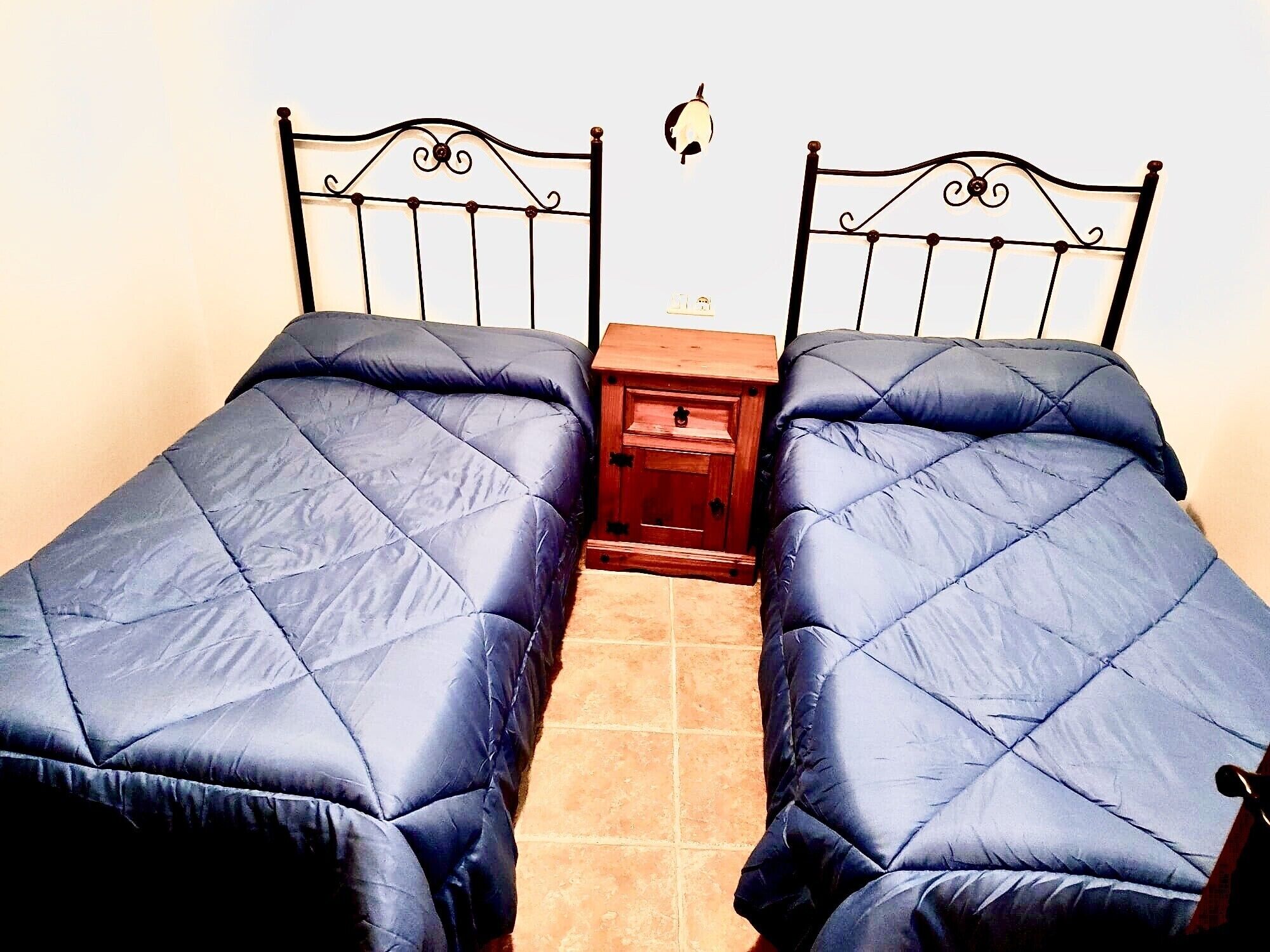 Ein Zimmer mit zwei Betten, jeweils mit Kopfteil und Fußteil, und einem Nachttisch dazwischen.
